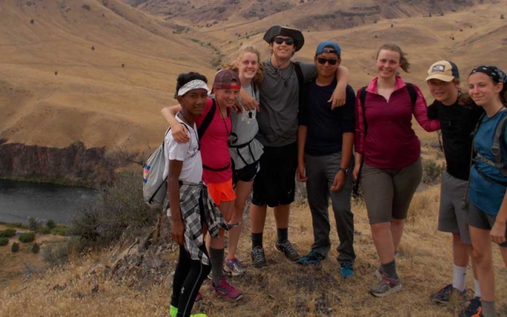 A group of students stand high above a river, wrapping their arms around each other and smile at the camera.